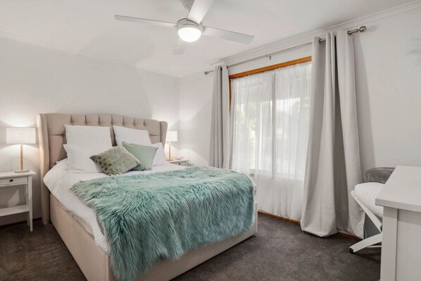 Ein ordentlich eingerichtetes Schlafzimmer mit Bett, Nachttischen, einem Schreibtisch und einem Deckenventilator.