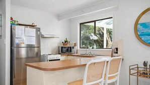 Une cuisine moderne dotée d’un îlot central, d’appareils électroménagers en acier inoxydable et offrant une vue sur l’extérieur.