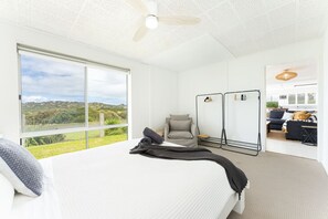 Ein Schlafzimmer mit einem großen Bett, einem Sessel, einem Kleiderschrank und Blick ins Freie.