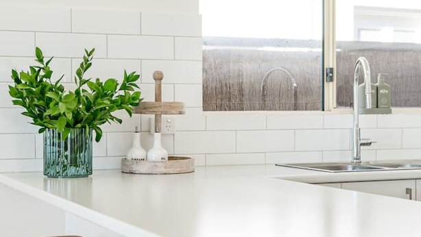 A modern kitchen with a white countertop, a large window, and a bar area with stools.