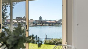 A view from a room with a large window overlooking a lake, with houses in the background.
