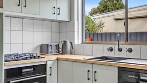Una cocina moderna con armarios blancos, estufa a gas, lavavajillas y ventana con vista a una cerca y árboles.