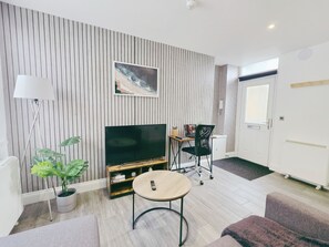 Ein modernes Wohnzimmer mit Flachbildfernseher, Couchtisch aus Holz und schwarzem Bürostuhl.