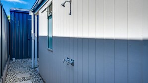 Un couloir extérieur étroit, avec une porte donnant sur une pièce dotée d’une fenêtre et d’une douche.
