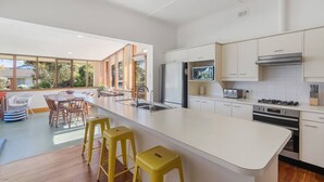 Une cuisine moderne dotée d’un grand îlot central, d’appareils électroménagers en acier inoxydable et offrant une vue sur l’extérieur.