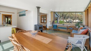 Une cuisine moderne dotée d’un îlot central, d’un coin repas avec une table en bois et d’un espace salon confortable avec des meubles en osier.