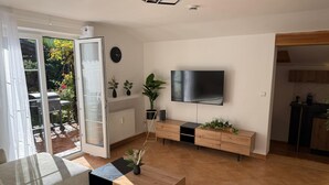 Un salon moderne avec un téléviseur, des meubles en bois, une porte vitrée donnant sur un patio et un coin cuisine.