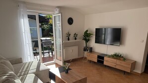 Un salon comprenant un canapé, une table basse, un téléviseur et une porte-fenêtre coulissante donnant sur un espace extérieur.