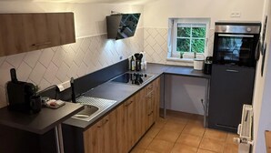 Une cuisine moderne avec un plan de travail noir, des meubles en bois, un four encastré et une fenêtre donnant sur un paysage verdoyant.