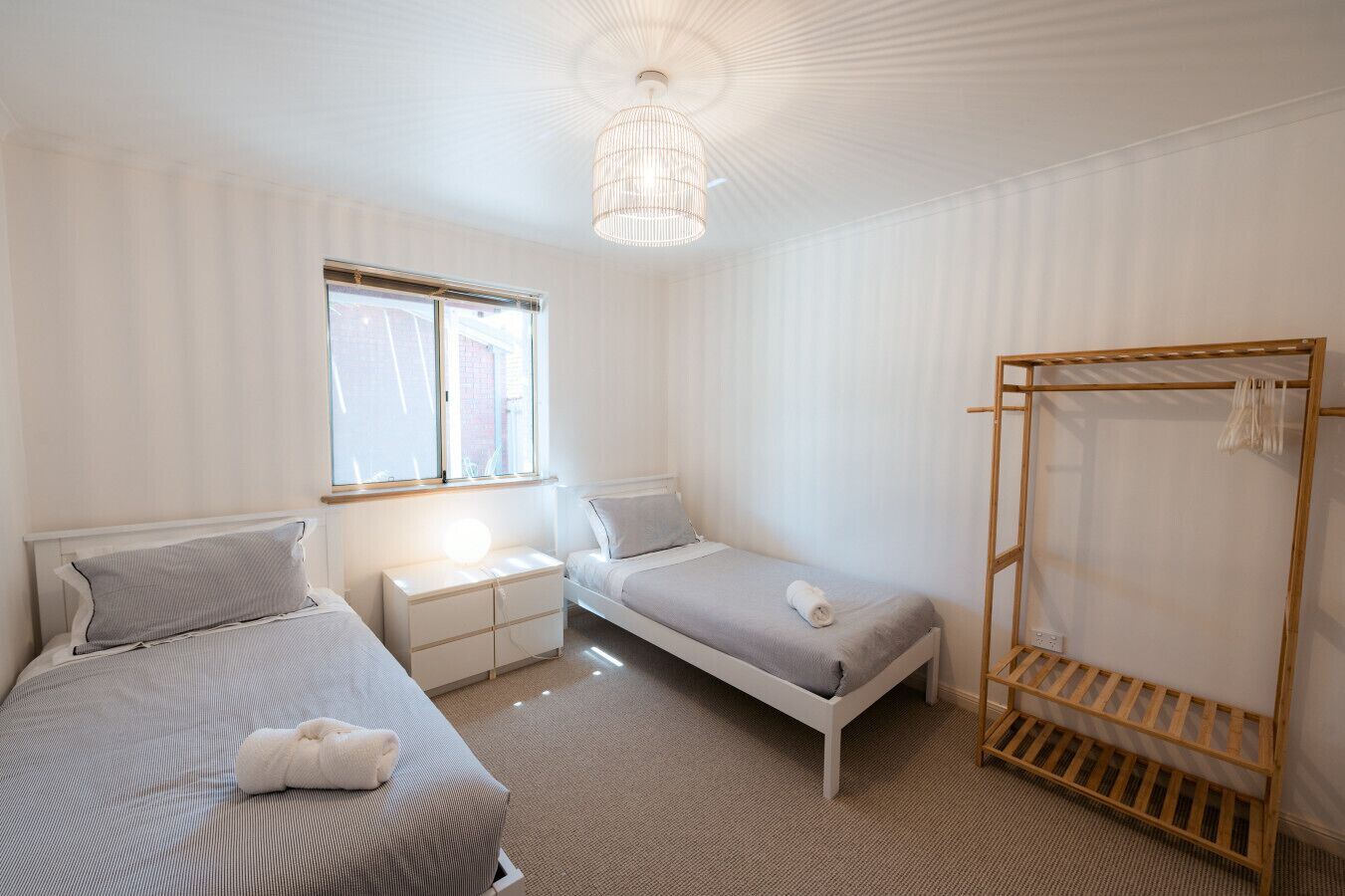 Une chambre avec deux lits, une armoire en bois, une table de chevet et une fenêtre.