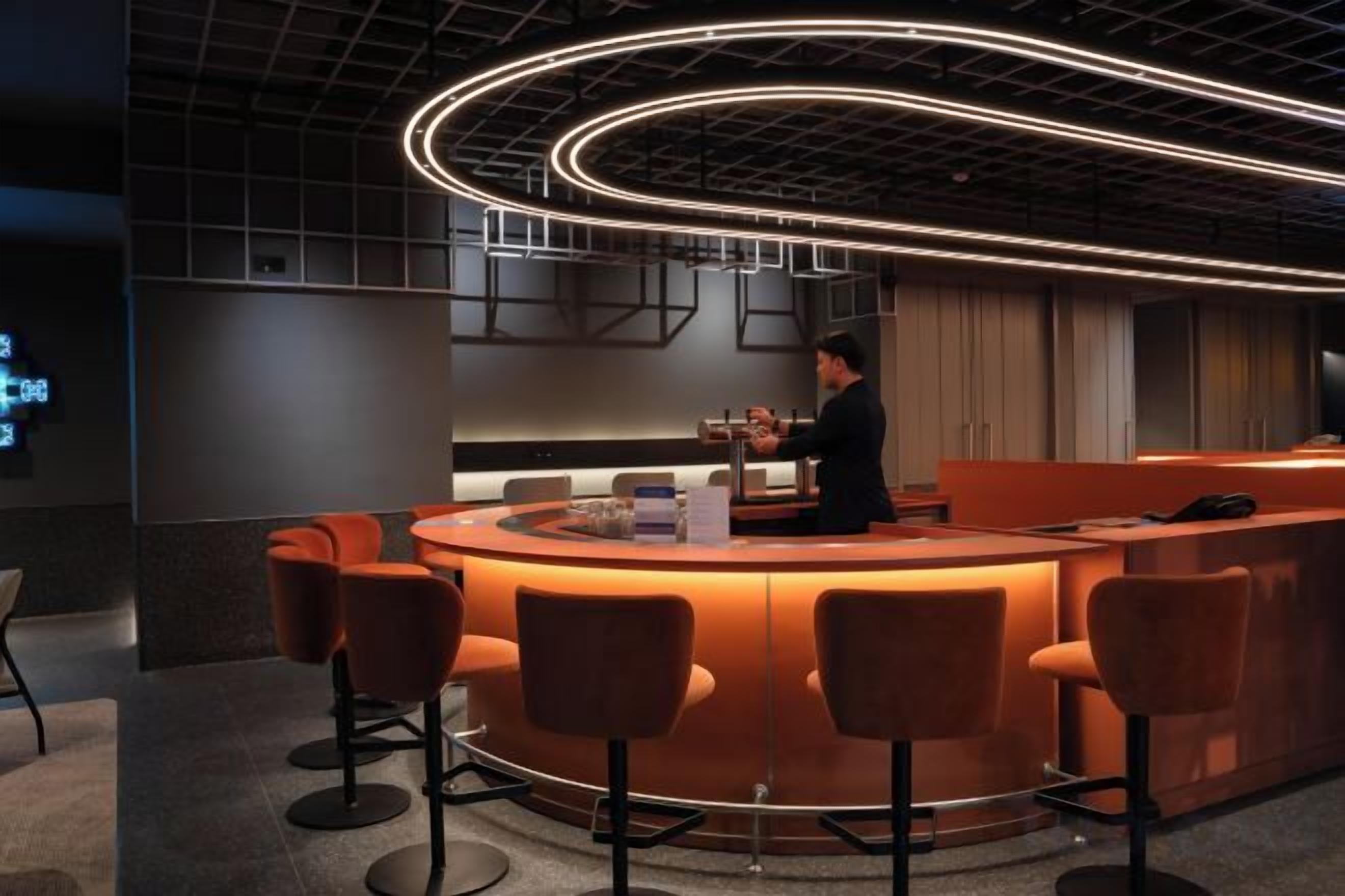 Un espace bar avec un comptoir incurvé, des tabourets de bar et une personne debout derrière le comptoir.