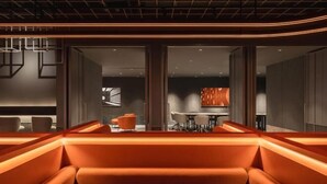A modern interior with orange seating, a dining area, and a visible kitchen in the background. - CapsuleTransit MAX - Terminal 2 (Sepang)