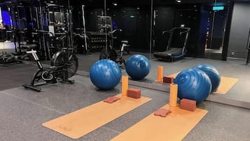 Une salle de sport équipée de matériel d’exercice, de tapis de yoga et de grands ballons de gymnastique.