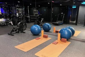 Un gimnasio con equipo de ejercicio, colchonetas de yoga y pelotas de ejercicios grandes.