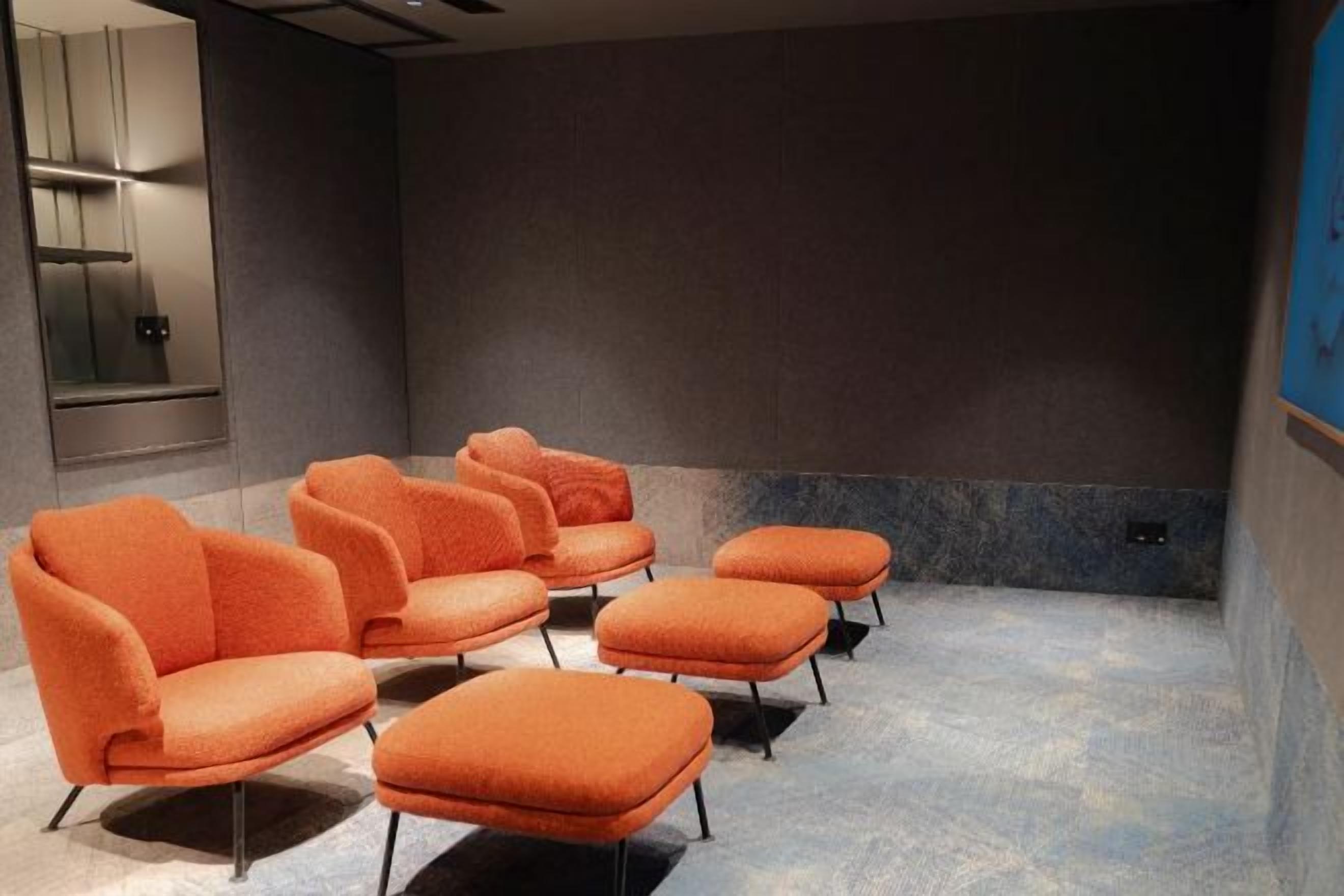 Una habitación con una fila de sillas anaranjadas y una pantalla grande, probablemente para presentaciones o proyecciones de películas.