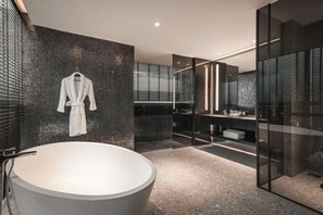 Un baño moderno con una bañera grande, una bata colgada y un área de ducha con mampara de vidrio.