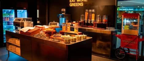 A food station with a sign that reads 'EAT MORE GREENS' and a popcorn cart.