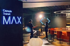 A modern lounge area with a neon sign, bar seating, and a unique wall design. - CapsuleTransit MAX - Terminal 2 (Sepang)