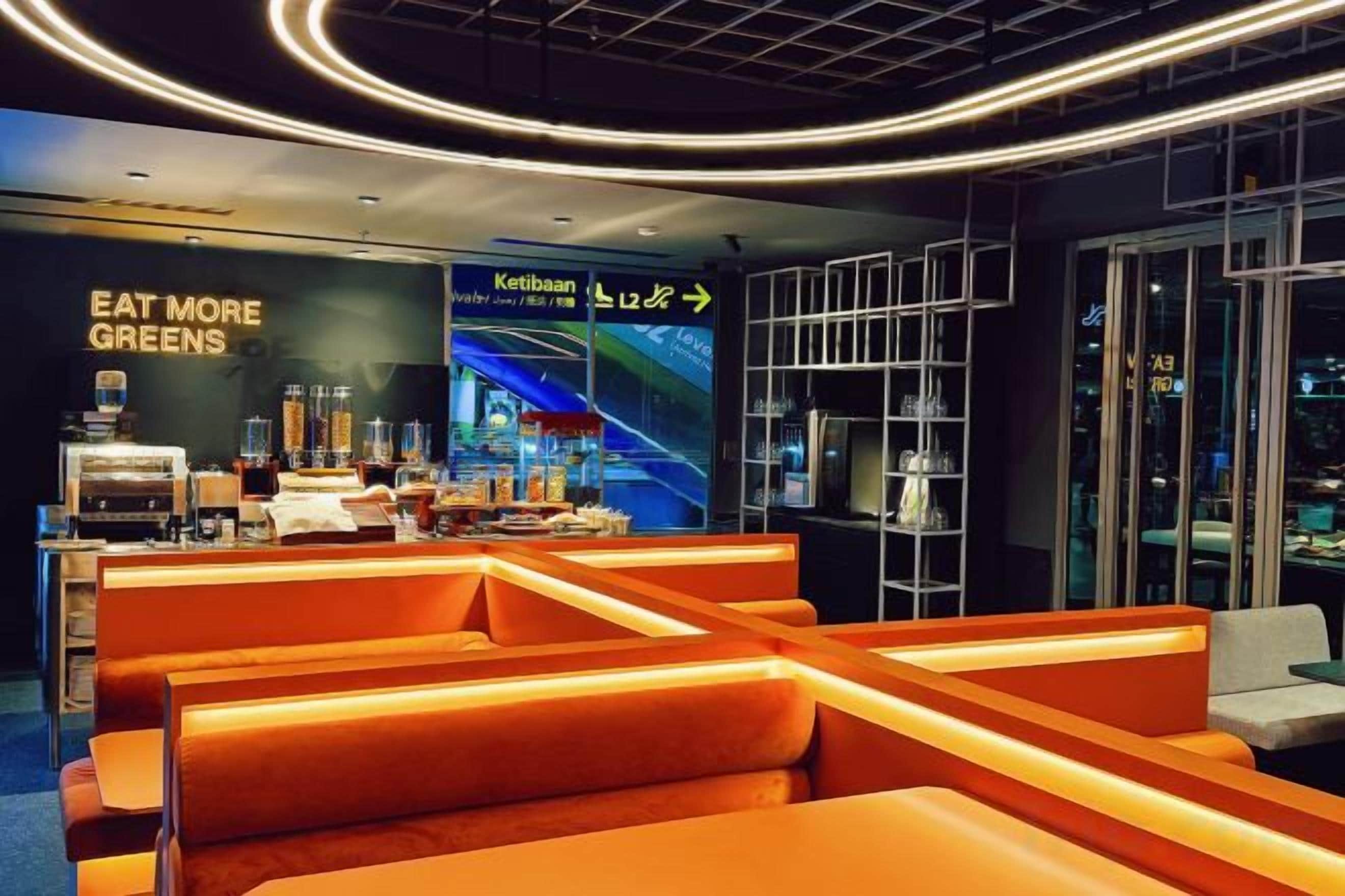 A modern restaurant with orange seating and a sign that reads 'EAT MORE GREENS.'