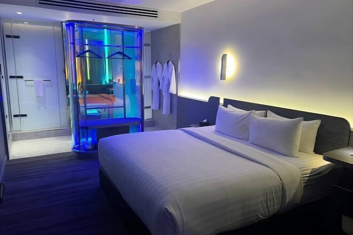 Una camera d'albergo con un letto, cabina doccia in vetro e luce a parete.