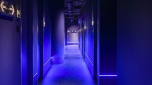 A hallway with a blue-lit floor and walls, leading to a door at the end. - CapsuleTransit MAX - Terminal 2 (Sepang)