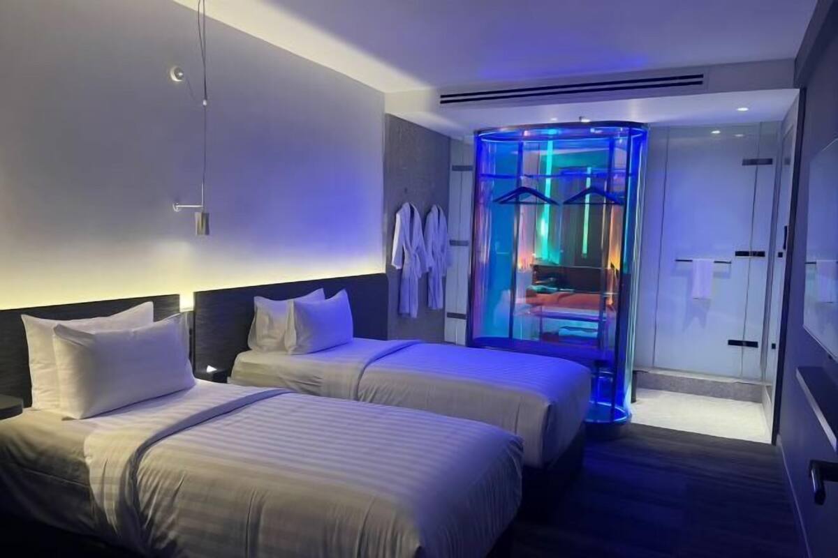 Una moderna camera d'albergo con due letti, un ascensore in vetro e vista sull'interno.