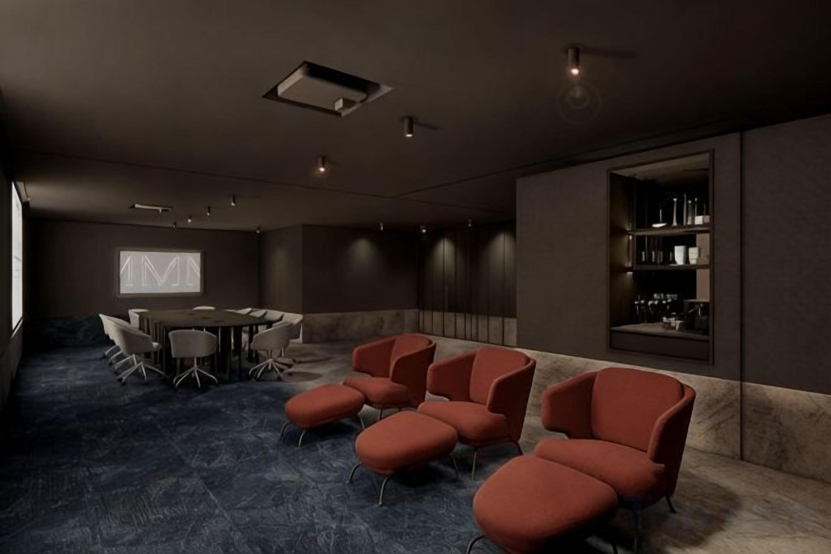 A conference room with a round table, red chairs, a projector screen, and a bookshelf.