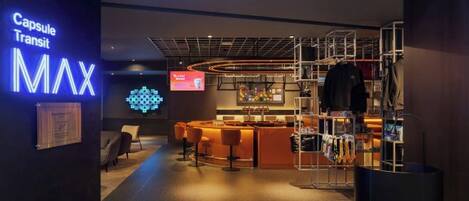 A modern interior with a Capsule Transit MAX sign, a bar area with stools, and a clothing rack.