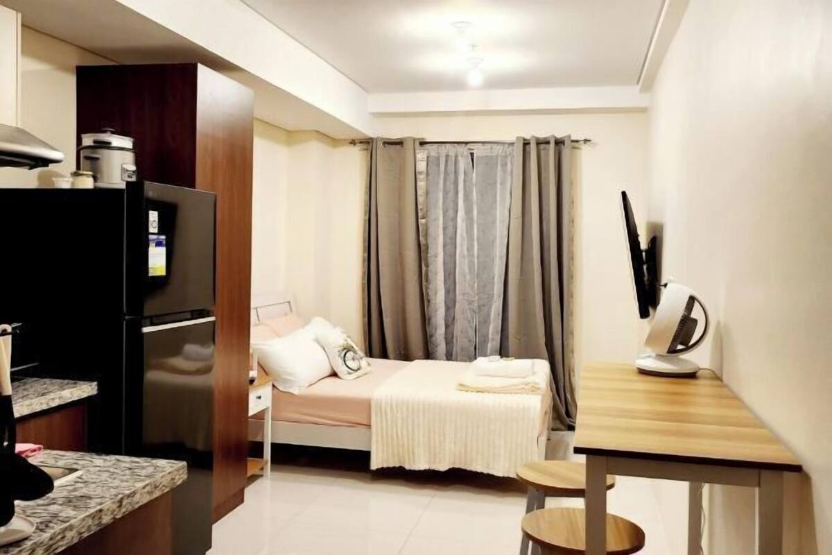 Ein kleines Zimmer mit Bett, Tisch, Schreibtisch, einer Mikrowelle und einem Kühlschrank.