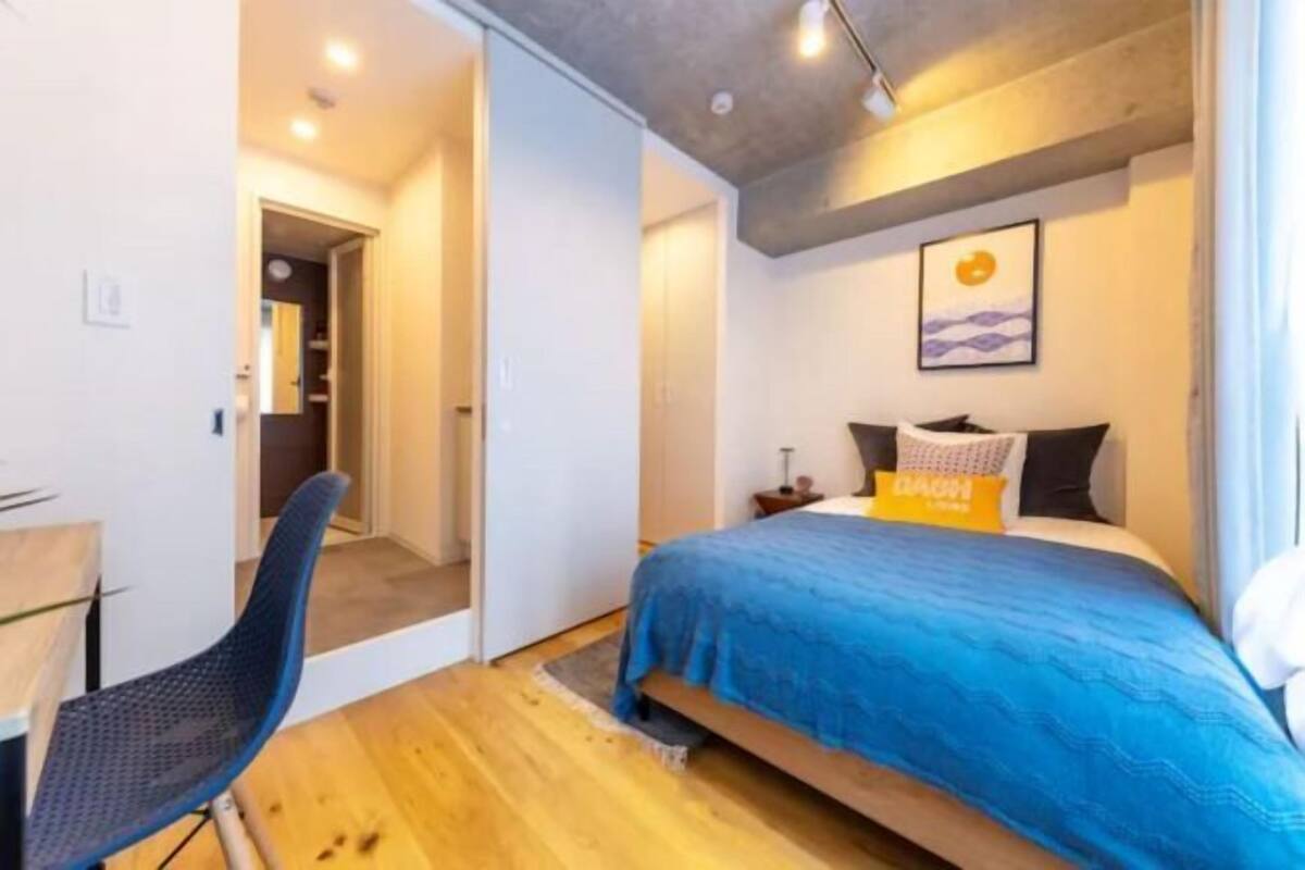 A bedroom with a bed, a desk, and a chair. There is a door leading to another room.