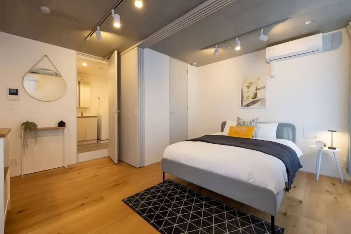 A modern bedroom with a large bed, a bedside table, a mirror, and a wall-mounted air conditioning unit.