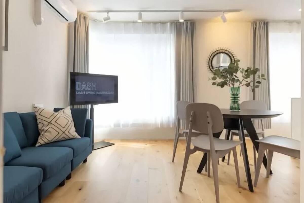 A modern living room with a blue sofa, a dining table with chairs, a flat-screen TV, and a decorative mirror.