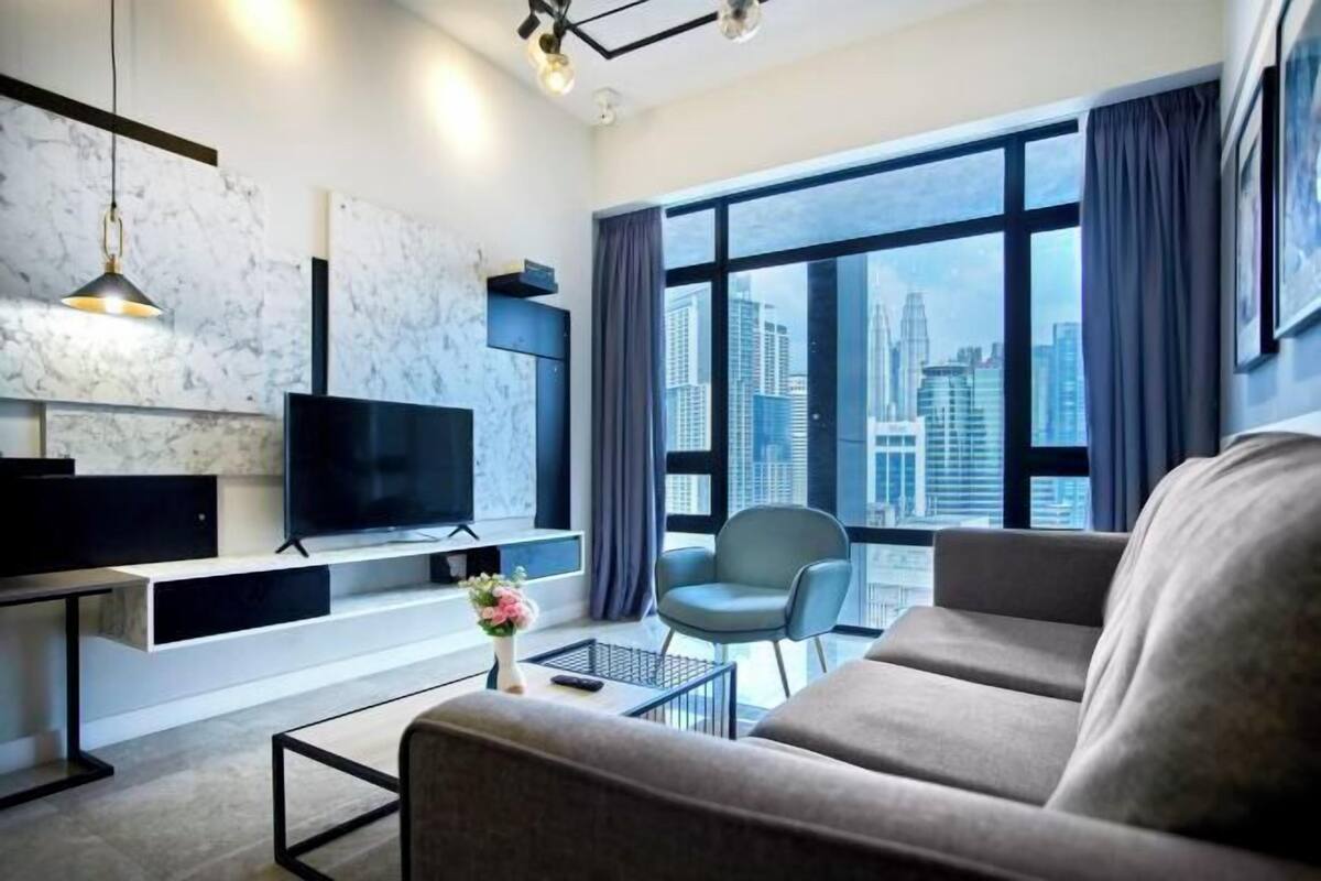 Una sala de estar moderna con un ventanal grande, un televisor de pantalla plana, un sofá, una silla y una mesa de centro.