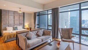 Una habitación de hotel moderna con cama, sofá, sillón, ventanas amplias y vistas a la ciudad.
