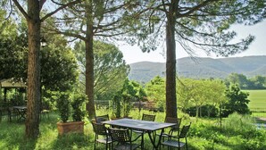 Un área de comedor al aire libre con una mesa y sillas rodeada de árboles, con vistas a un paisaje pintoresco con colinas en la distancia.