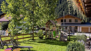 Eine Holzhütte mit Spielbereich, umgeben von üppigem Grün und einem Bergpanorama.