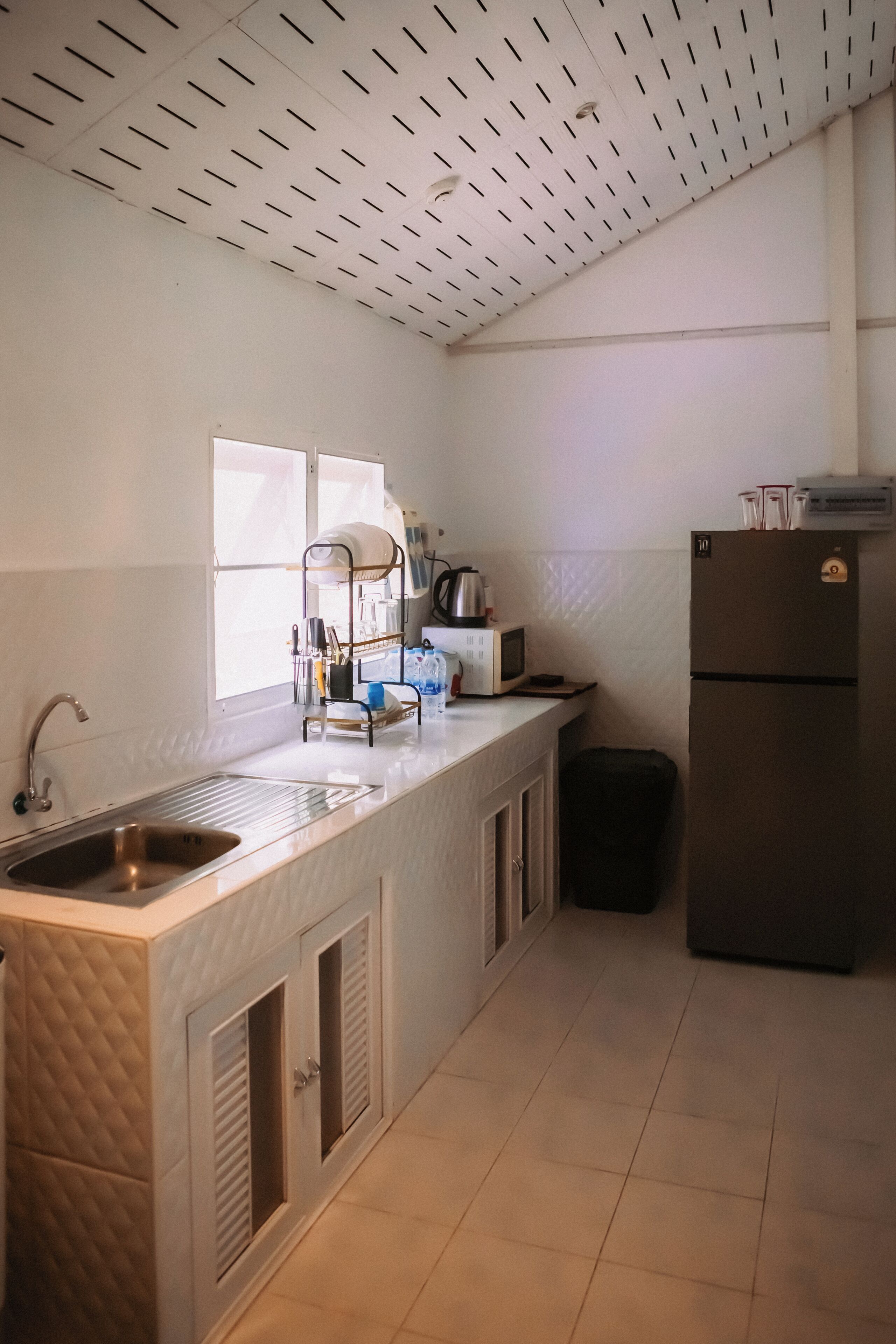 A kitchen with a stainless steel sink, a microwave, a refrigerator, and a window providing natural light.