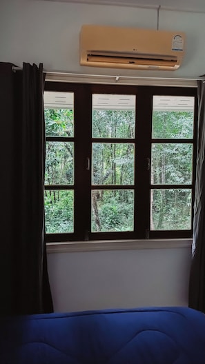 A room with a bed, a window with curtains, and an air conditioning unit above the window.