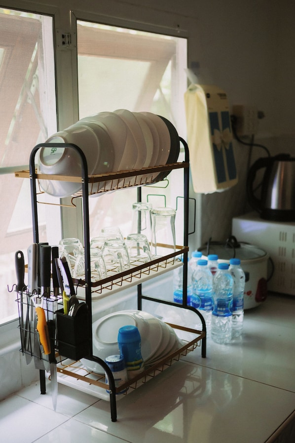 A kitchen with a rack holding dishes and glasses, a kettle, and water bottles.