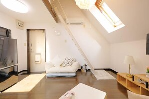 A modern loft-style room with a sloped ceiling, a sofa, a TV, a lamp, and a wooden floor. - Mi-Loft Shibuya (Tokyo)