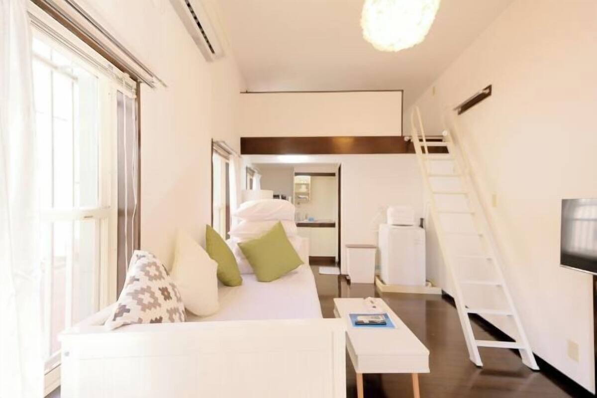 A modern hotel room with a sofa, a small table, a ladder, and a TV.