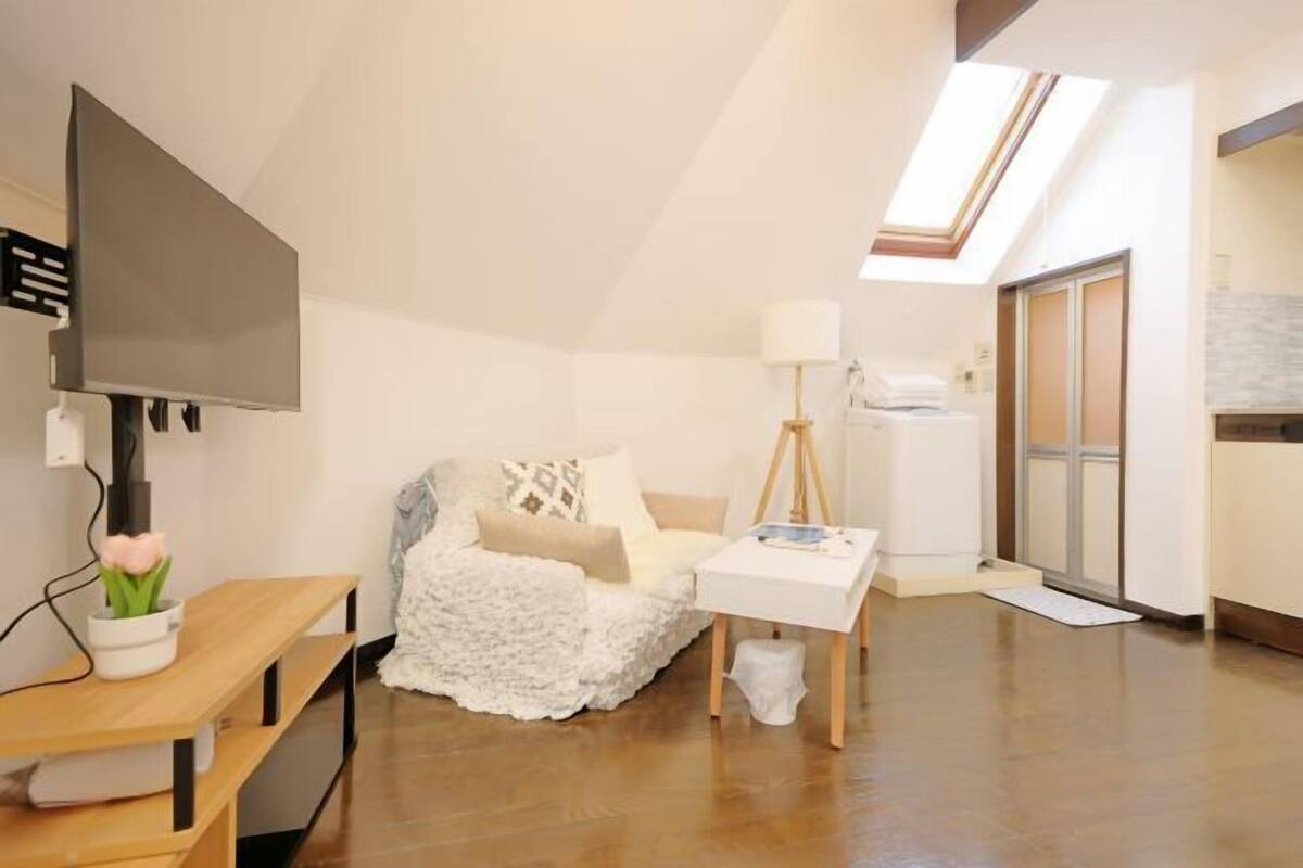 A modern living room with a flat-screen TV, a white sofa, a wooden bench, a small table, and a skylight.