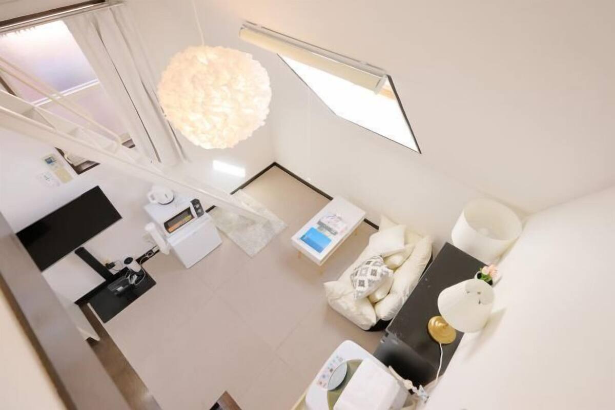 A modern, well-lit room with a large window, a white sofa, a small table, and a hanging light fixture.