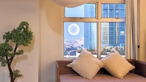 Ein Bett mit zwei Kissen, ein Fenster mit Blick auf die Stadt und eine Zimmerpflanze.