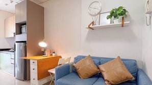 Ein modernes Wohnzimmer mit blauem Sofa, Holztisch und einer kleinen Küchenzeile.
