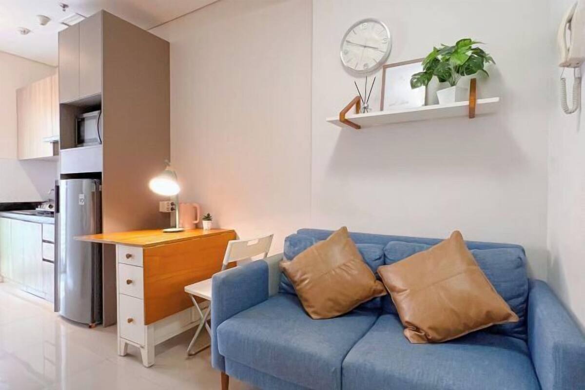 Een moderne woonkamer met een blauwe bank, een houten bureau en een klein keukenhoekje.