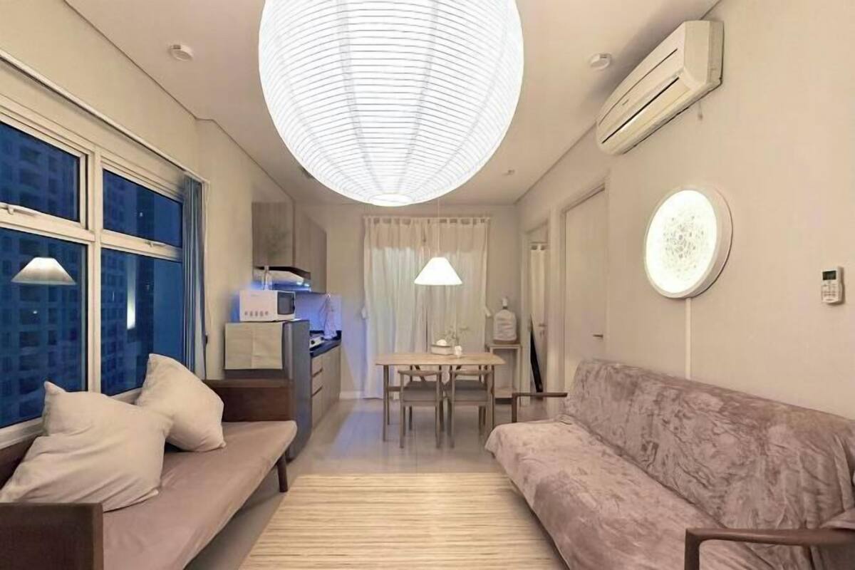 Een moderne hotelkamer met een bank, een eettafel, een kitchenette en een grote ronde plafondlamp.