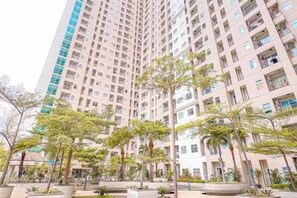 Een hoog appartementencomplex met meerdere balkons, omgeven door aangelegde groene zones met bomen.