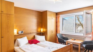 Quarto com cama, mesa de cabeceira, cadeira e janela com vista.