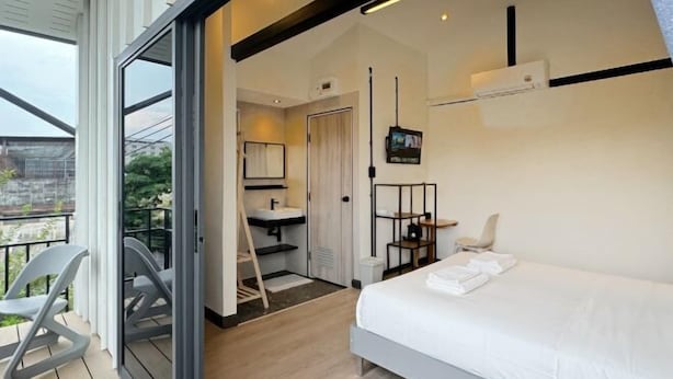 Een moderne hotelkamer met een bed, een badkamer met een wastafel en spiegel, een televisie en een balkon met stoelen.